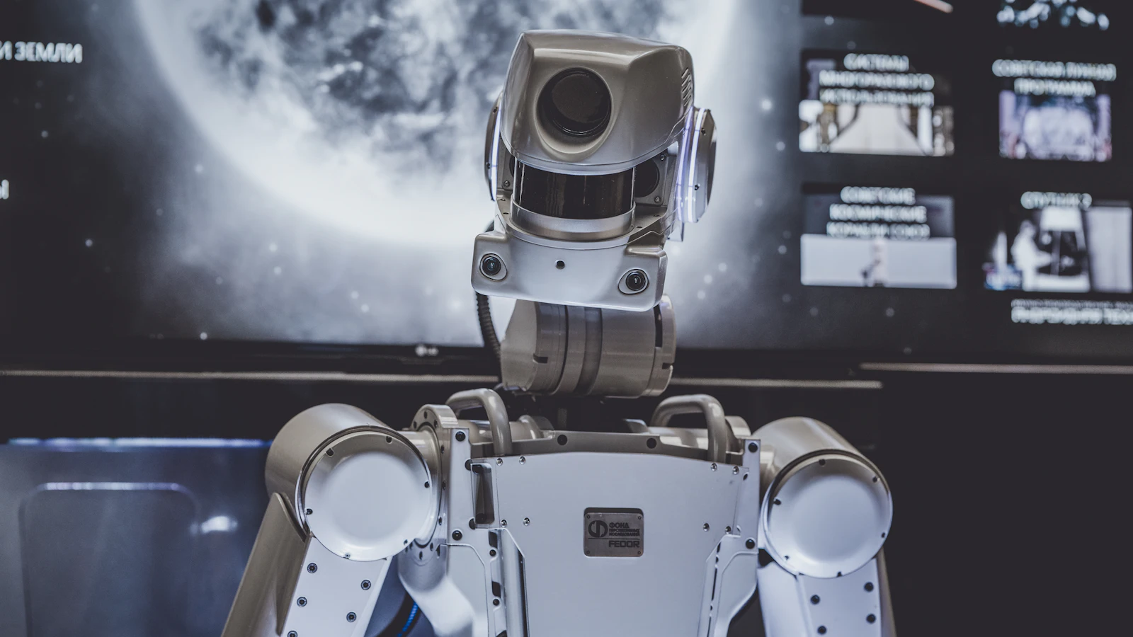 Close-up of a humanoid robot's mechanical head and camera housing in front of a dark screen.